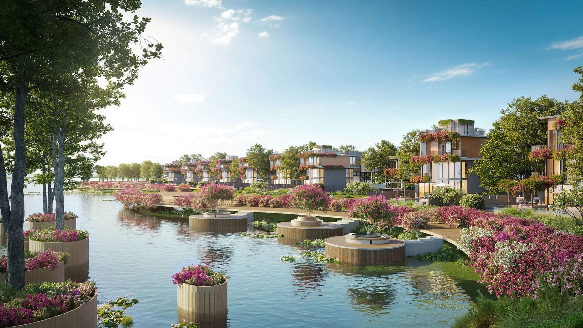 Hình ảnh một khu biệt thự ven sông tại Alluvia City, với những ngôi nhà hiện đại được bao quanh bởi cây xanh và hoa hồng phấn rực rỡ. Một con sông uốn lượn chảy qua, với các bồn hoa nổi trên mặt nước và những cây cầu gỗ nhỏ bắc ngang, tạo nên khung cảnh thanh bình và sang trọng dưới bầu trời xanh trong.