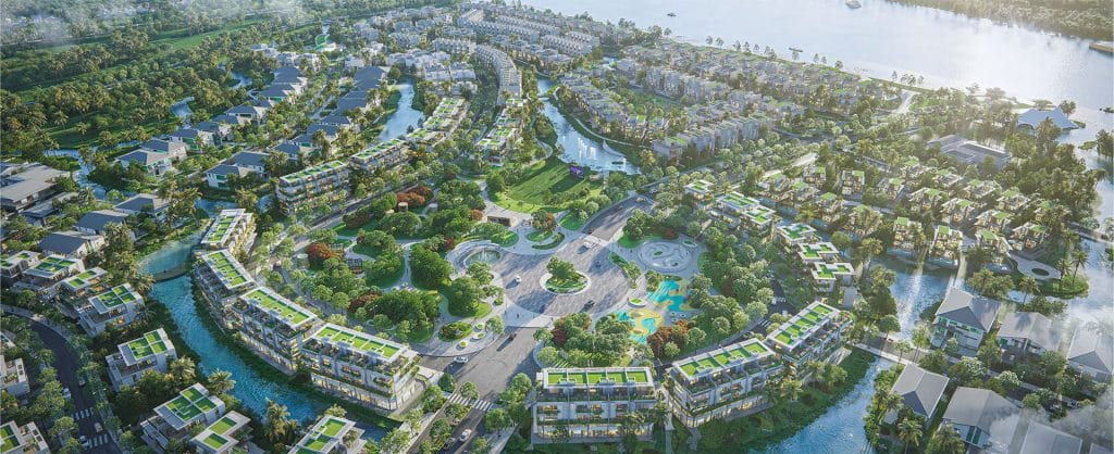 Bất Động Sản Hưng Yên Qua Lăng Kính Alluvia City 5 Hình ảnh toàn cảnh dự án Alluvia City từ trên cao, thể hiện một khu đô thị hiện đại với các tòa nhà mái xanh, đường phố uốn lượn, công viên trung tâm và dòng sông chảy qua, bao quanh bởi cây cối và không gian xanh mát. Một hồ nước lớn nằm ở phía bên phải, phản chiếu ánh sáng mặt trời, tạo nên khung cảnh hài hòa giữa thiên nhiên và kiến trúc.
