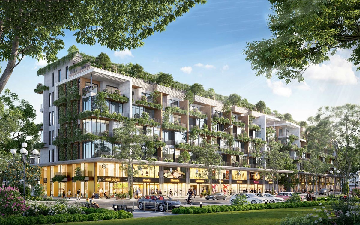 Alluvia City Văn Giang 15 Hình ảnh của dãy shophouse tại Alluvia City, với mặt tiền kính lớn, các cửa hàng sôi động, và các tầng trên phủ cây xanh, bao quanh bởi cây cối và không gian công cộng.