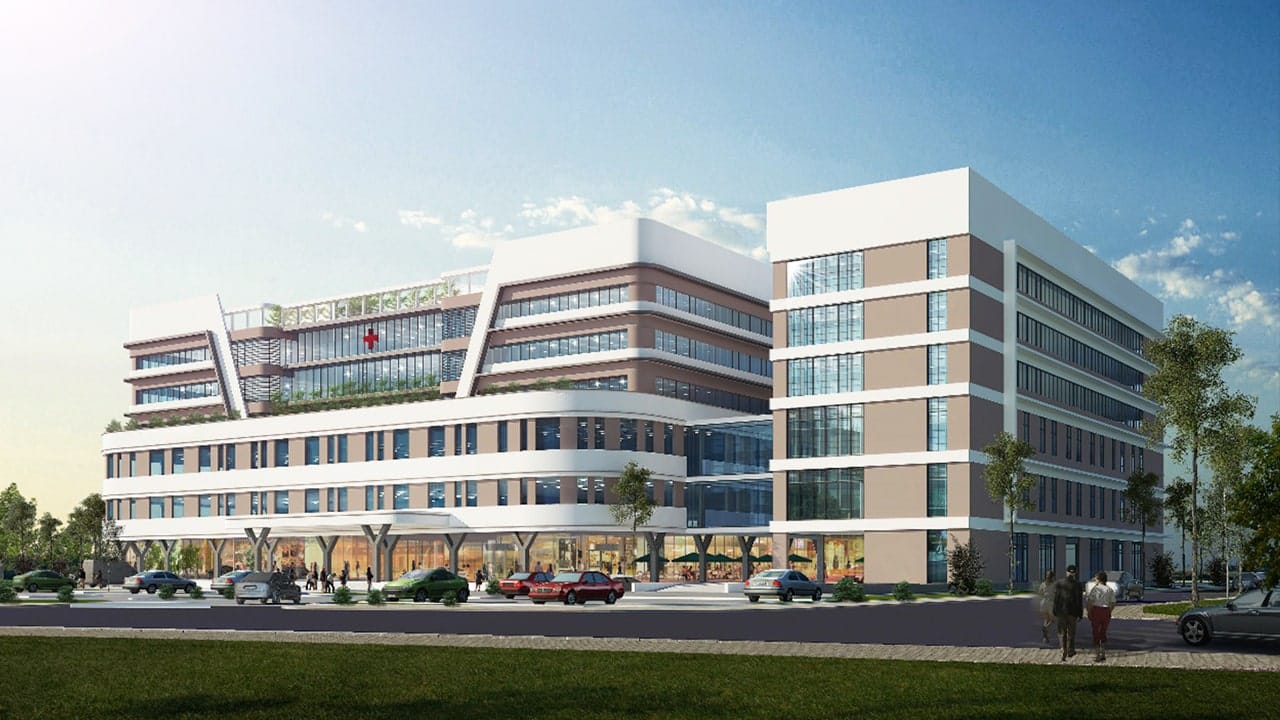 Hình ảnh phối cảnh bệnh viện đa khoa hiện đại tại Alluvia City, với tòa nhà cao tầng thiết kế khối vuông vức, mặt kính rộng, khuôn viên xanh và bãi đỗ xe phía trước.
